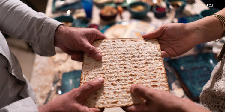 Two people holding a large piece of matzah.