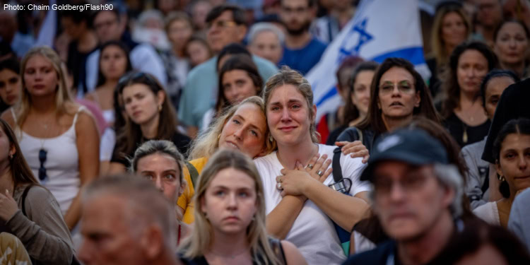 A crowd has a solemn moment, some hold Israeli flags.