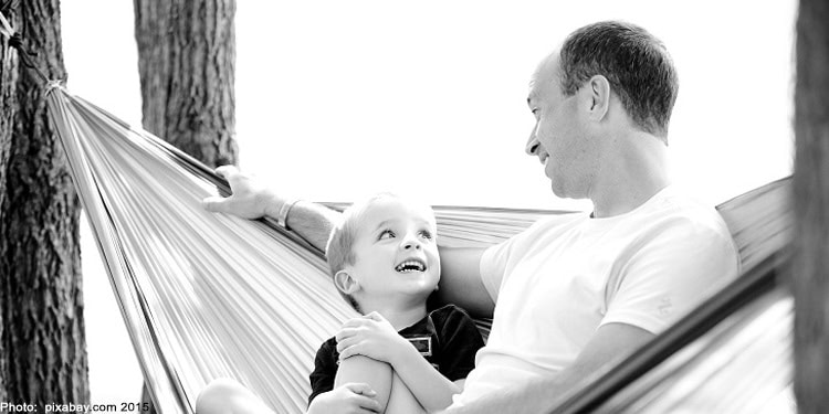 Black and white image of a father and son sitting in a hammock.