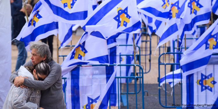 People mourn while huggging, surrounded by Israeli flags with the 