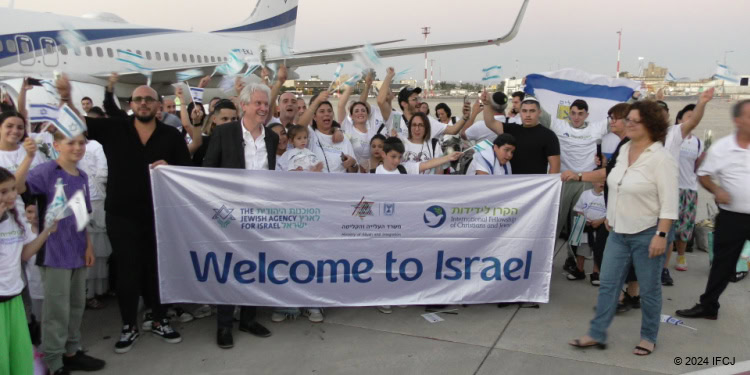 150 French olim arrive in Israel on a Fellowship aliyah flight. Crowd holds a Fellowship sign saying "Welcome To Israel"