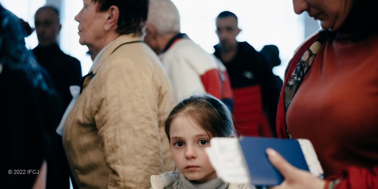 Young girl standing in the middle of a large crowd of people looking directly at the camera.