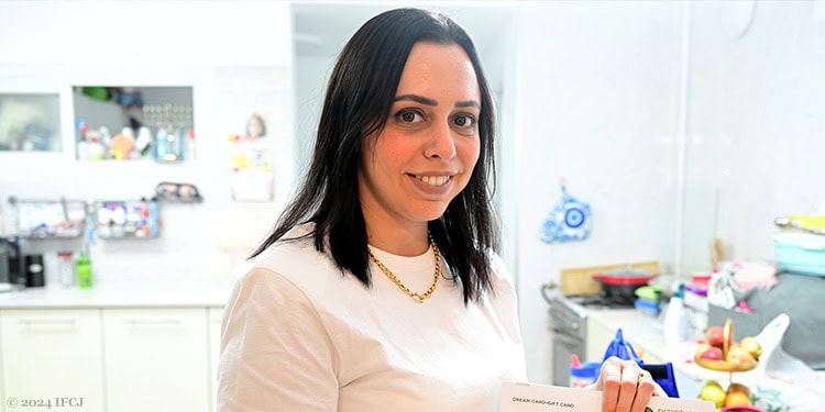 Young woman in kitchen wearing a white shirt smiling.