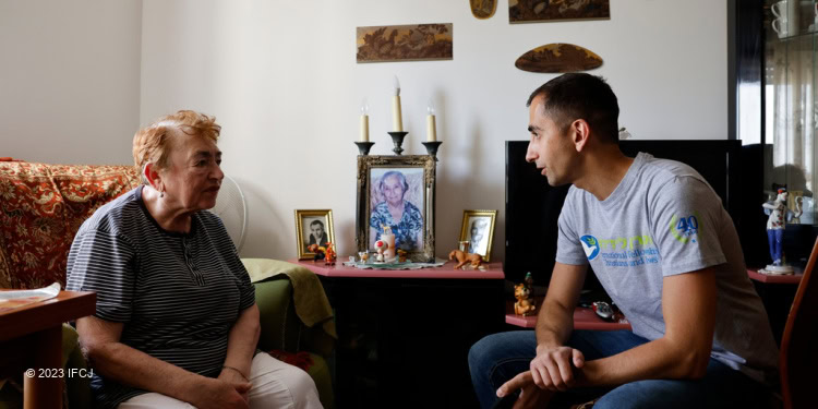 Young man wearing a shirt with IFCJ logo sits across from an elderly woman.