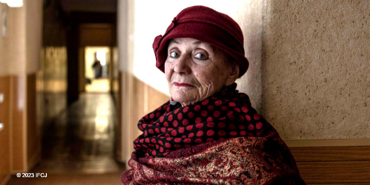 elderly woman stand in hallway, red hat, patterned scarf